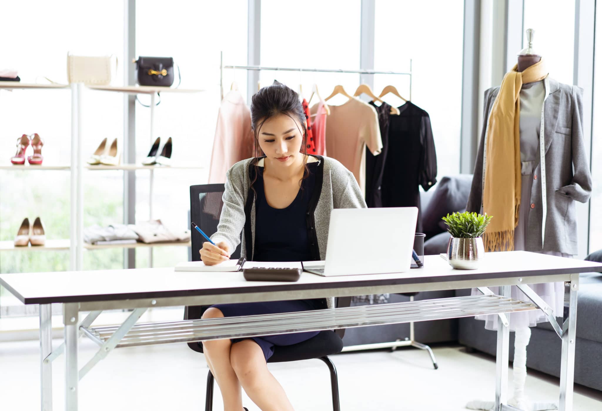 Young business Asian woman sitting at table and taking notes in notebook on table is laptop in clothes shop. Startup Small Business Owner Concept.; Shutterstock ID 1419827879; Purchase Order: ADI